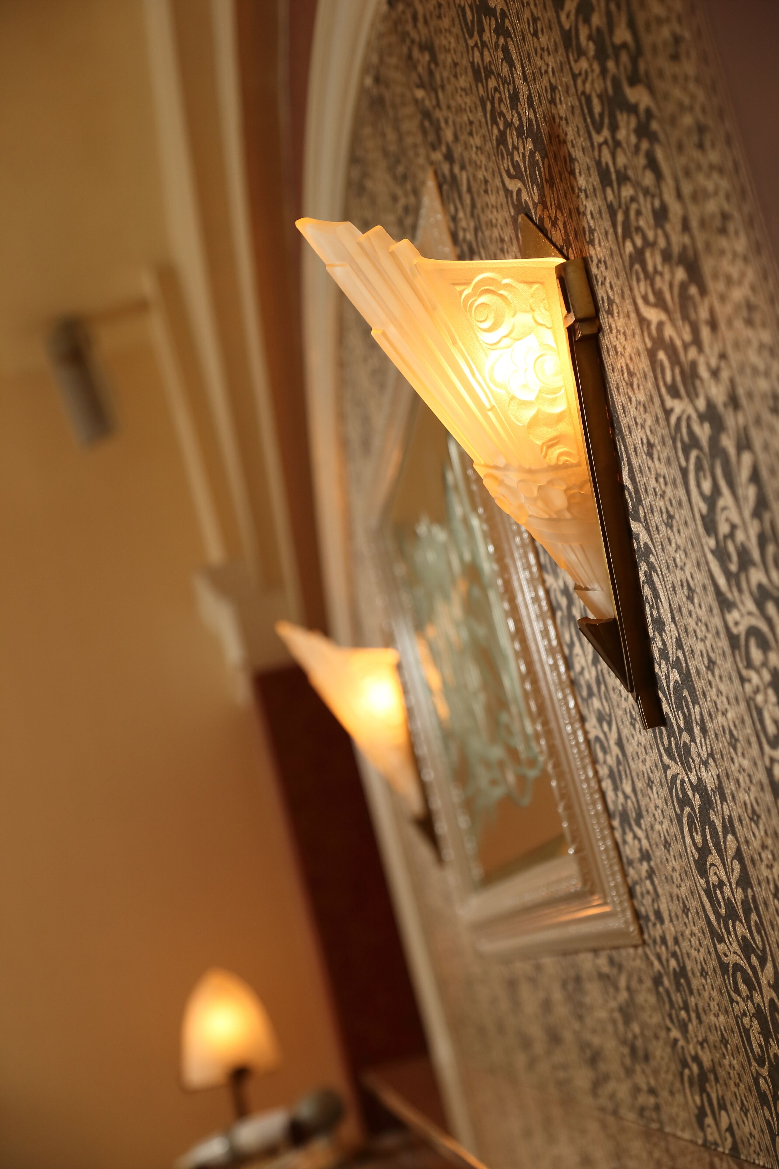 A wall-mounted light fixture with a decorative design, positioned next to a patterned wall.