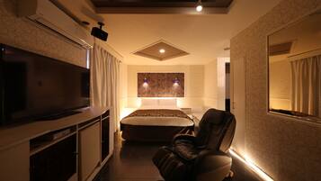 Een moderne hotelkamer met een flatscreen televisie, een massagestoel, een groot bed en een zithoekje.