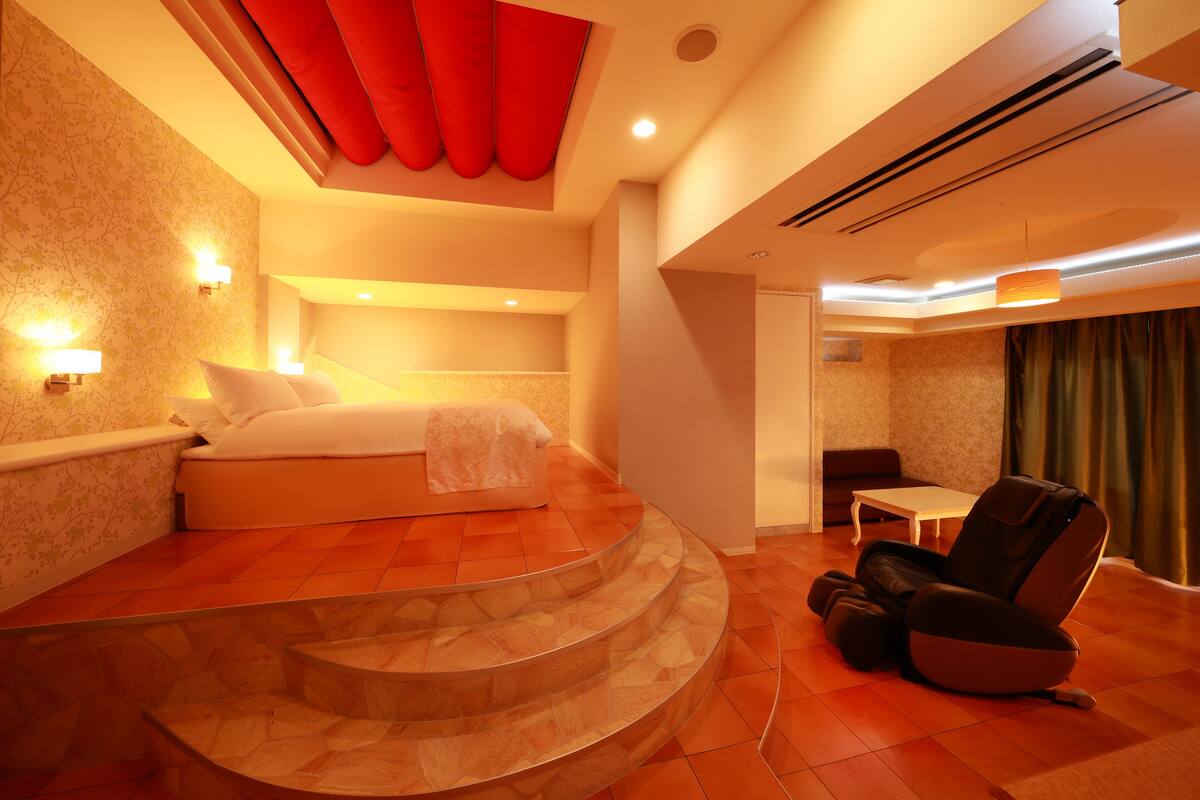 Une chambre d’hôtel moderne équipée d’un lit, d’un fauteuil massant et d’une petite table.