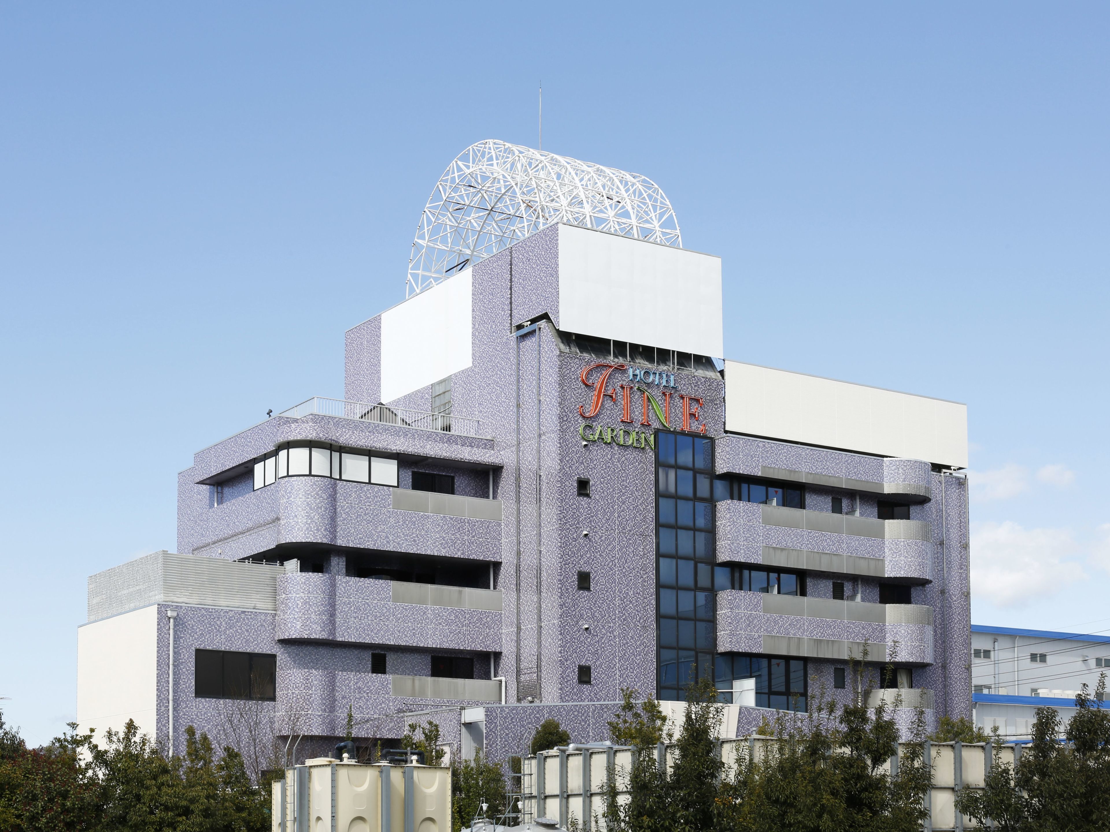 A hotel with a unique geodesic dome structure on top, a prominent sign reading "HOTEL FINE GARDEN," and a modern architectural design with multiple balconies.