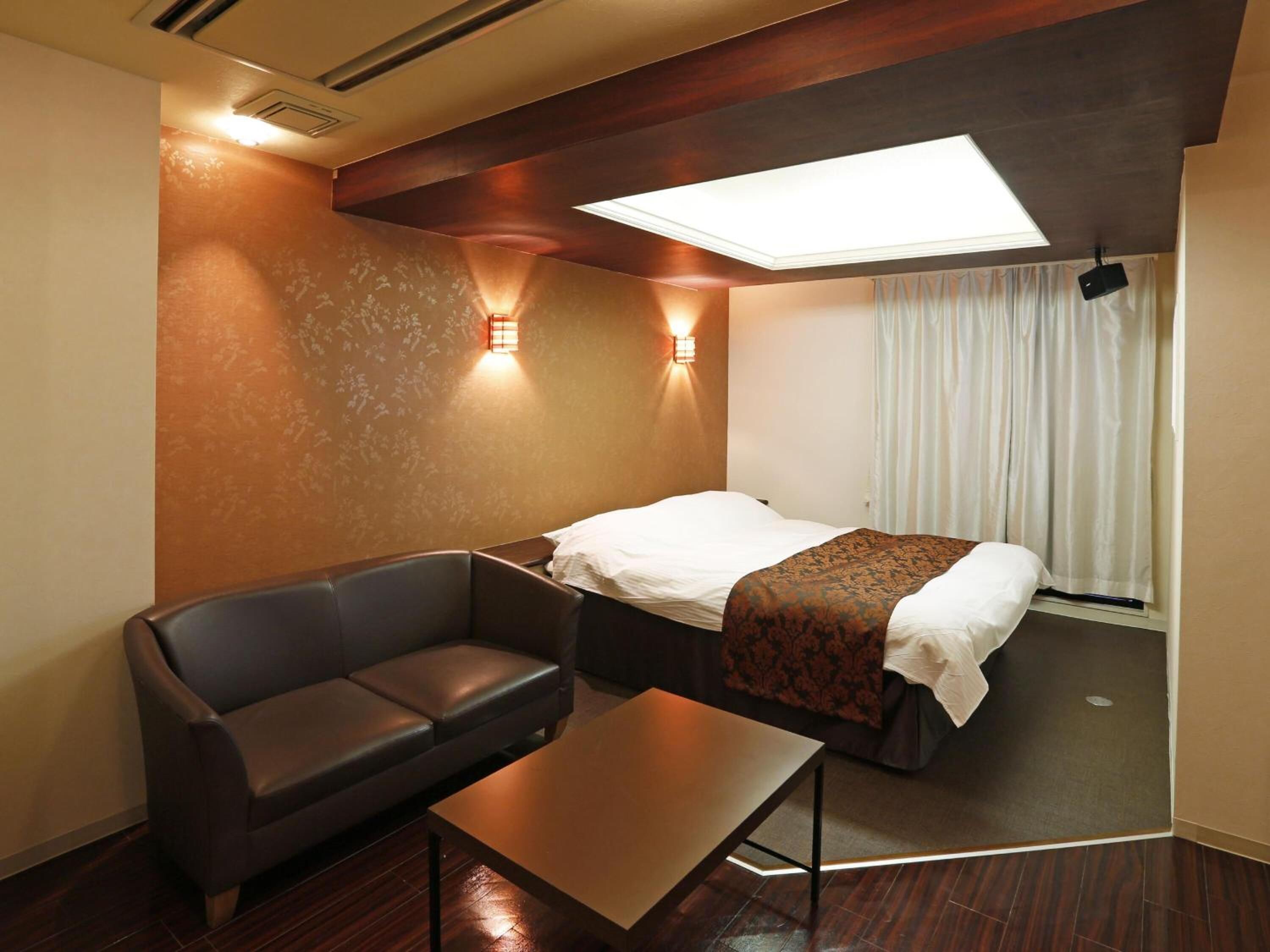A hotel room with a bed, a sofa, a table, and a ceiling light.