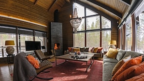Un salon chaleureux avec une cheminée, des sièges confortables et de grandes fenêtres donnant sur la forêt.