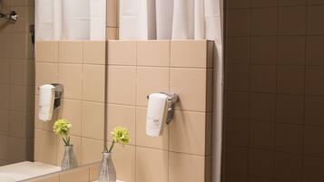 A bathroom with a white sink, two vases with flowers, a towel rack, and a mirror reflecting the shower curtain.