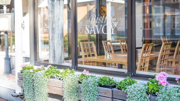 A restaurant with a sign reading "Bistro no SAVOY" and wooden outdoor seating visible through the window. - Hotel Savoy (Mariehamn)