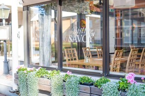A restaurant with a sign reading "Bistro no SAVOY" and wooden outdoor seating visible through the window. - Hotel Savoy (Mariehamn)