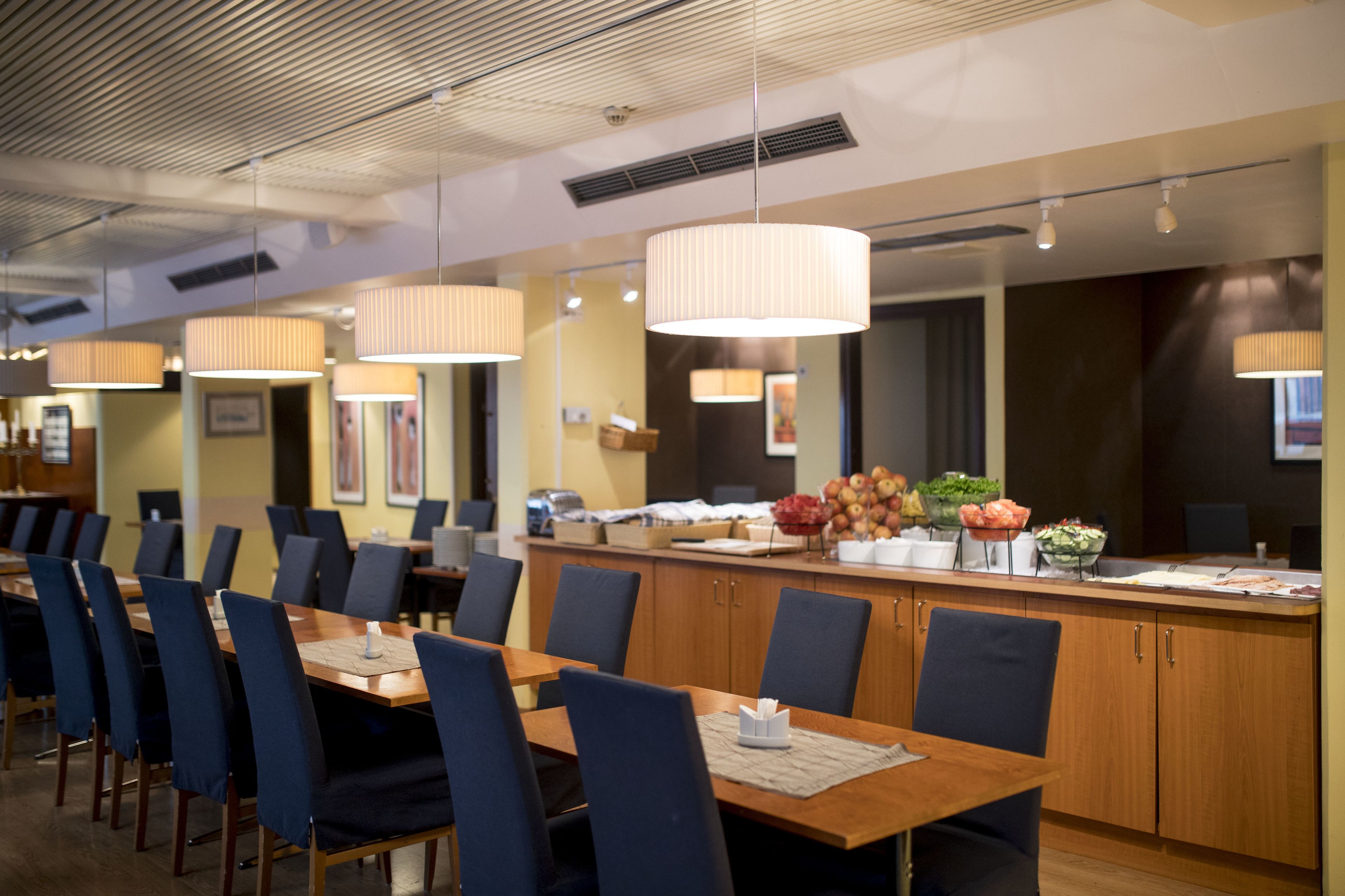 Comedor de hotel con largas mesas de madera, sillas azules y una isla central con comida y flores.