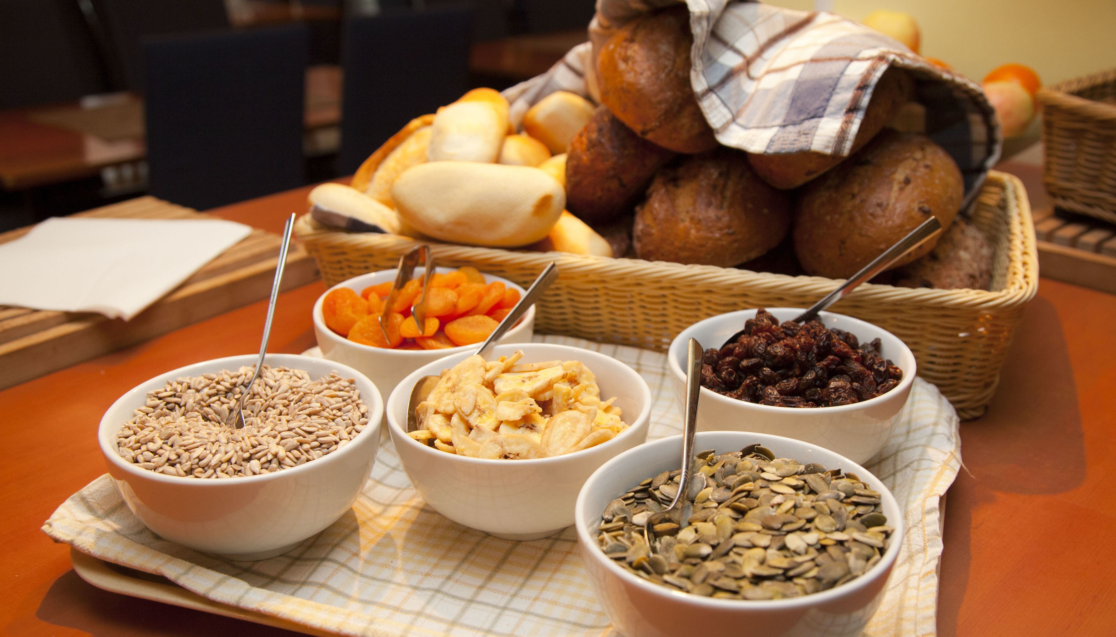 A table with various food items including bowls of seeds, dried fruits, and bread.
