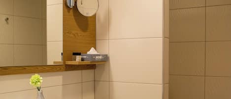 A modern bathroom with a white sink, mirror, and toilet. There is a towel hanging on the wall, a small vase with flowers, and a shelf with toiletries.