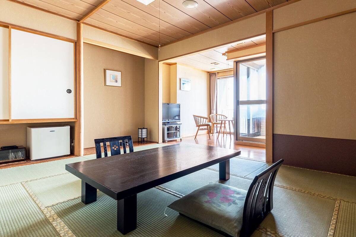 Ein traditioneller japanischer Raum mit Tatami-Böden, einem niedrigen Tisch und einem Fernseher.