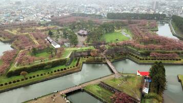 Vista aérea de um parque histórico com fosso, cerejeiras em flor e arquitetura tradicional.