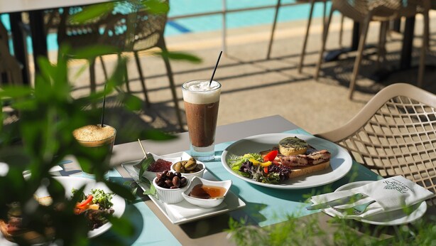 Ein Tisch mit einer Mahlzeit bestehend aus Salat, gegrilltem Fleisch und einem Getränk, draußen in der Nähe eines Pools.