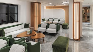 Eine moderne Hotelhalle mit einem grünen Sofa, grünen Sesseln, einem Holztisch und einer Holzwand.