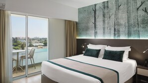 Ein Hotelzimmer mit einem großen Bett, Blick auf die Stadt durch eine Schiebetür und einem Bild an der Wand.