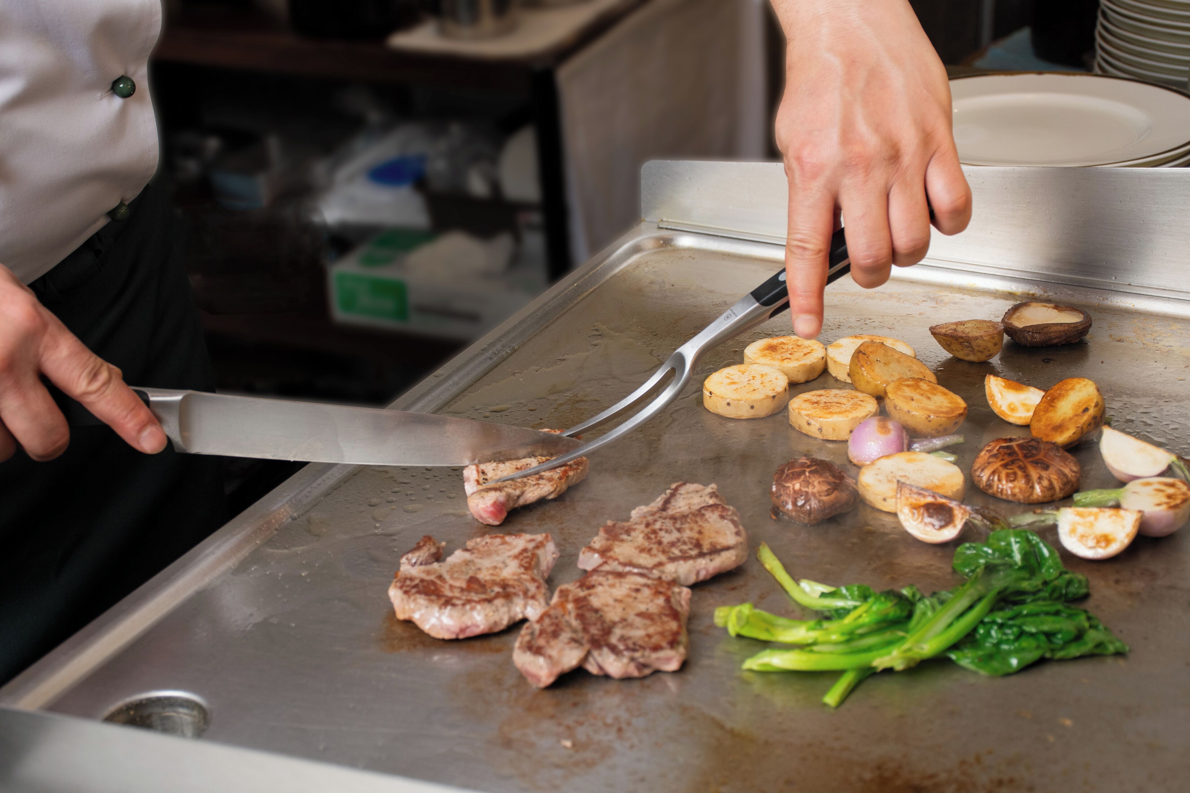 A person cooking on a grill with meat, potatoes, and vegetables.