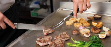 A person cooking on a grill with meat, potatoes, and vegetables.