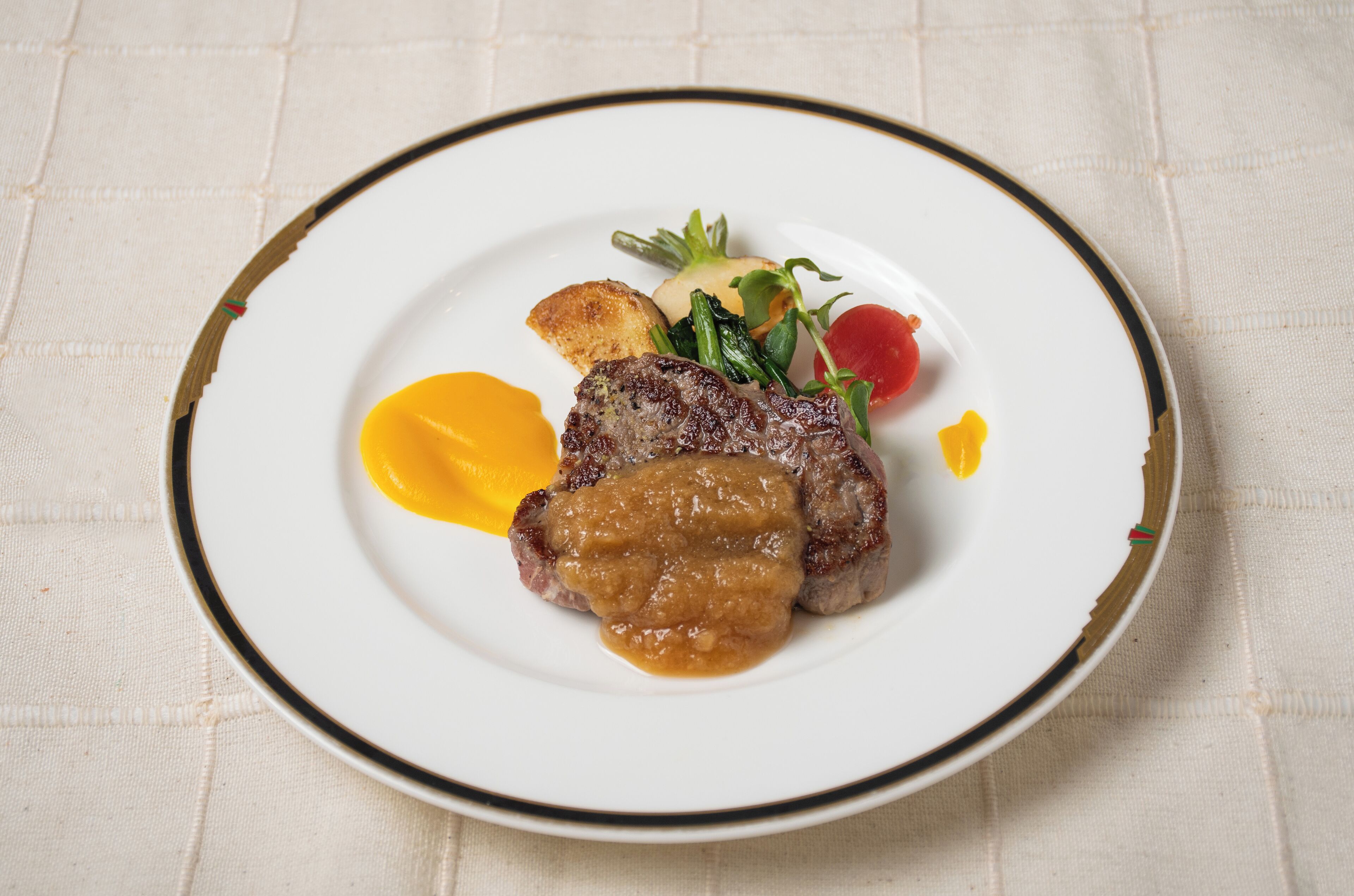 En tallerken mad med steak, grøntsager og sauce.