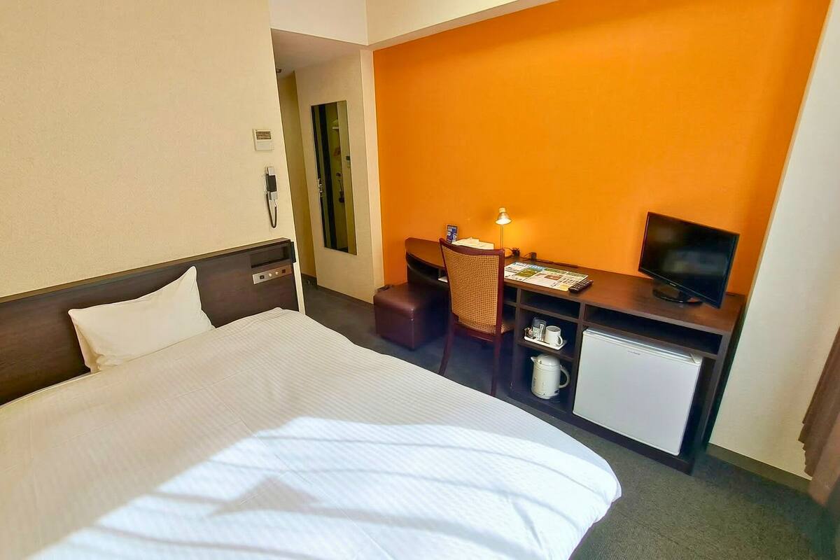 Una habitación de hotel con una cama, un escritorio con una silla, un televisor y un refrigerador pequeño.