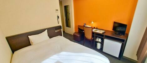 A hotel room with a bed, a desk with a chair, a television, and a small refrigerator.