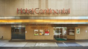 The exterior of Hotel Continental with a tiled facade, a glass entrance, and several promotional posters. - Hotel Continental (Fuchu)