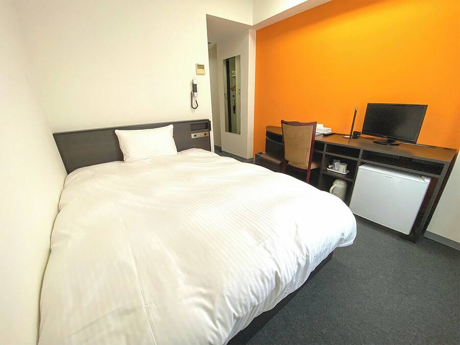 Ein Hotelzimmer mit einem großen Bett, einem Schreibtisch mit Computer, einer kleinen Kühlbox und einem Telefon.