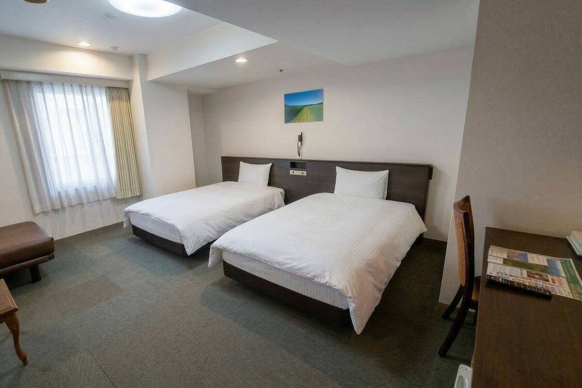 Habitación de hotel con dos camas, un escritorio, una silla, un sofá y un cuadro en la pared.
