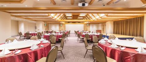 Una sala de conferencias con mesas redondas, sillas color beige y manteles rojos.