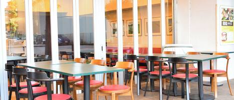 An indoor dining area with tables and chairs, large windows, and a poster on the wall.