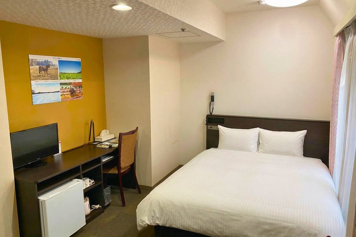 Habitación de hotel con cama, escritorio con computadora, silla y refrigerador pequeño.
