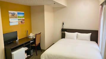 A hotel room with a bed, a desk with a computer, a chair, and a small refrigerator.