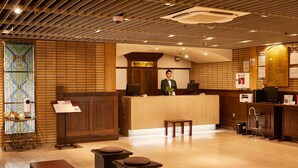 A reception area with a wooden reception desk, a reception sign, a reception attendant, and a wall-mounted menu board. - Hotel Continental (Fuchu)