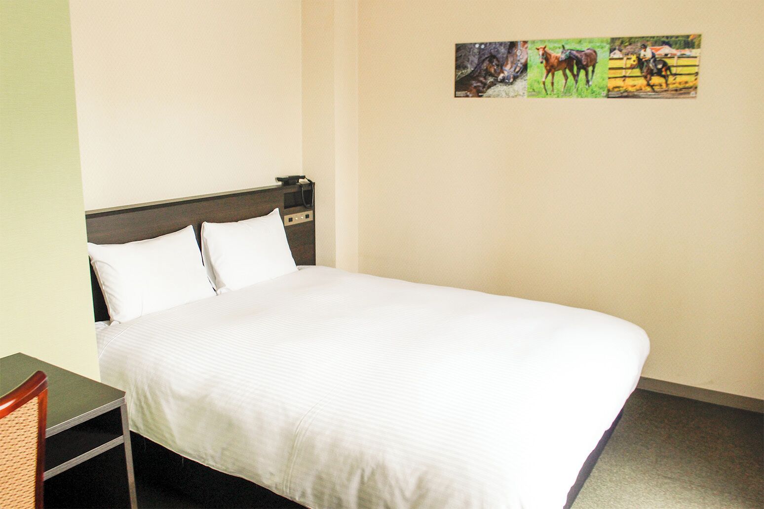 A hotel room with a bed, a nightstand, and a wall-mounted picture of horses.