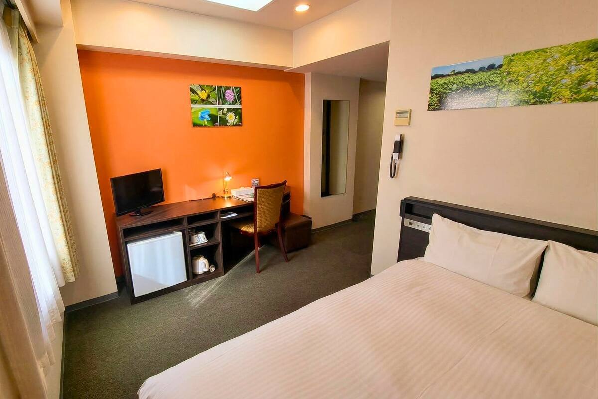 Habitación de hotel con cama, escritorio, silla, televisor y una kitchenette pequeña.