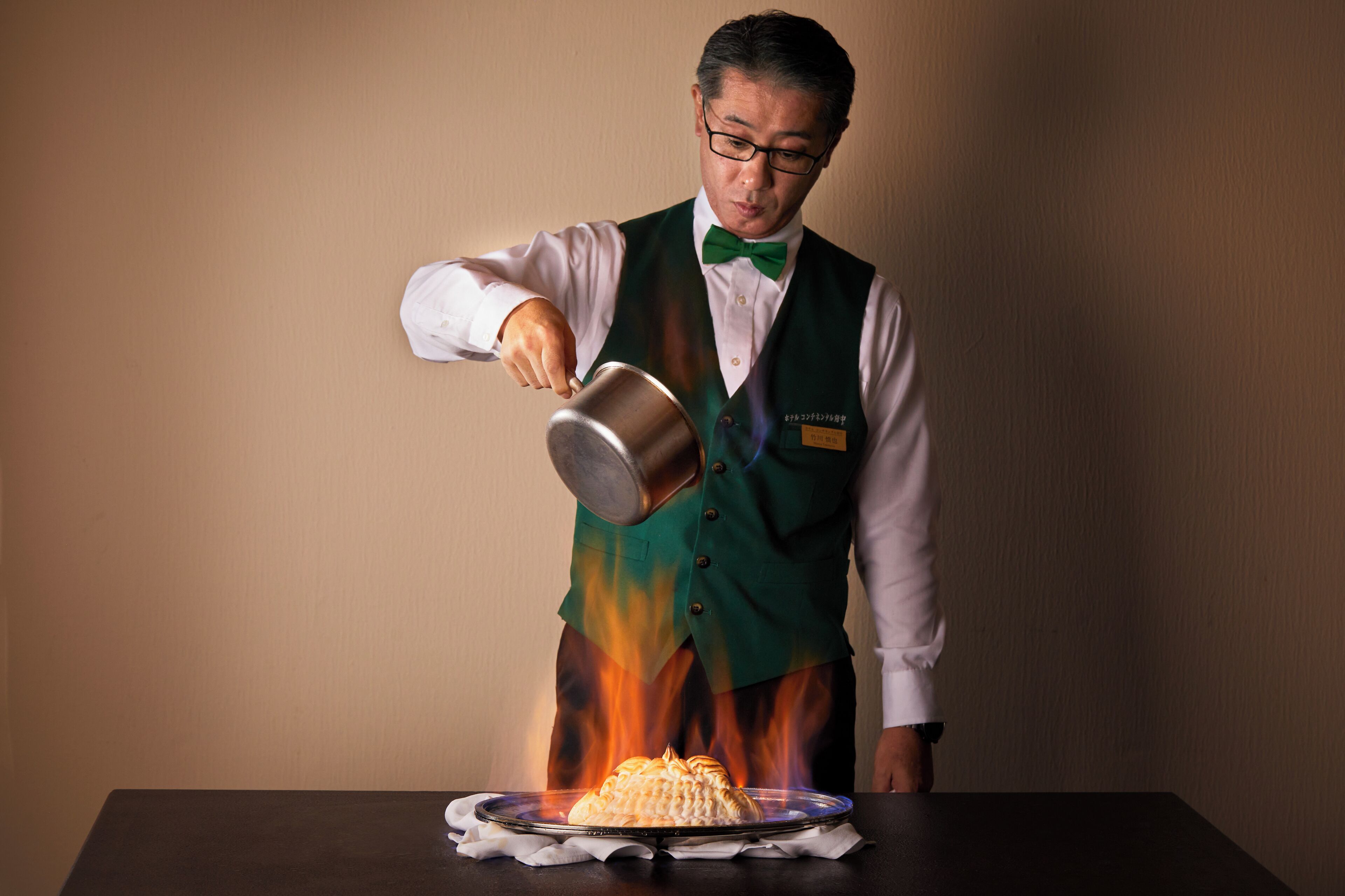 A person pouring a hot liquid onto a dish on a table.