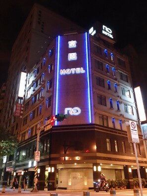 Un hotel con un letrero de neón llamativo, varios pisos y una entrada visible.