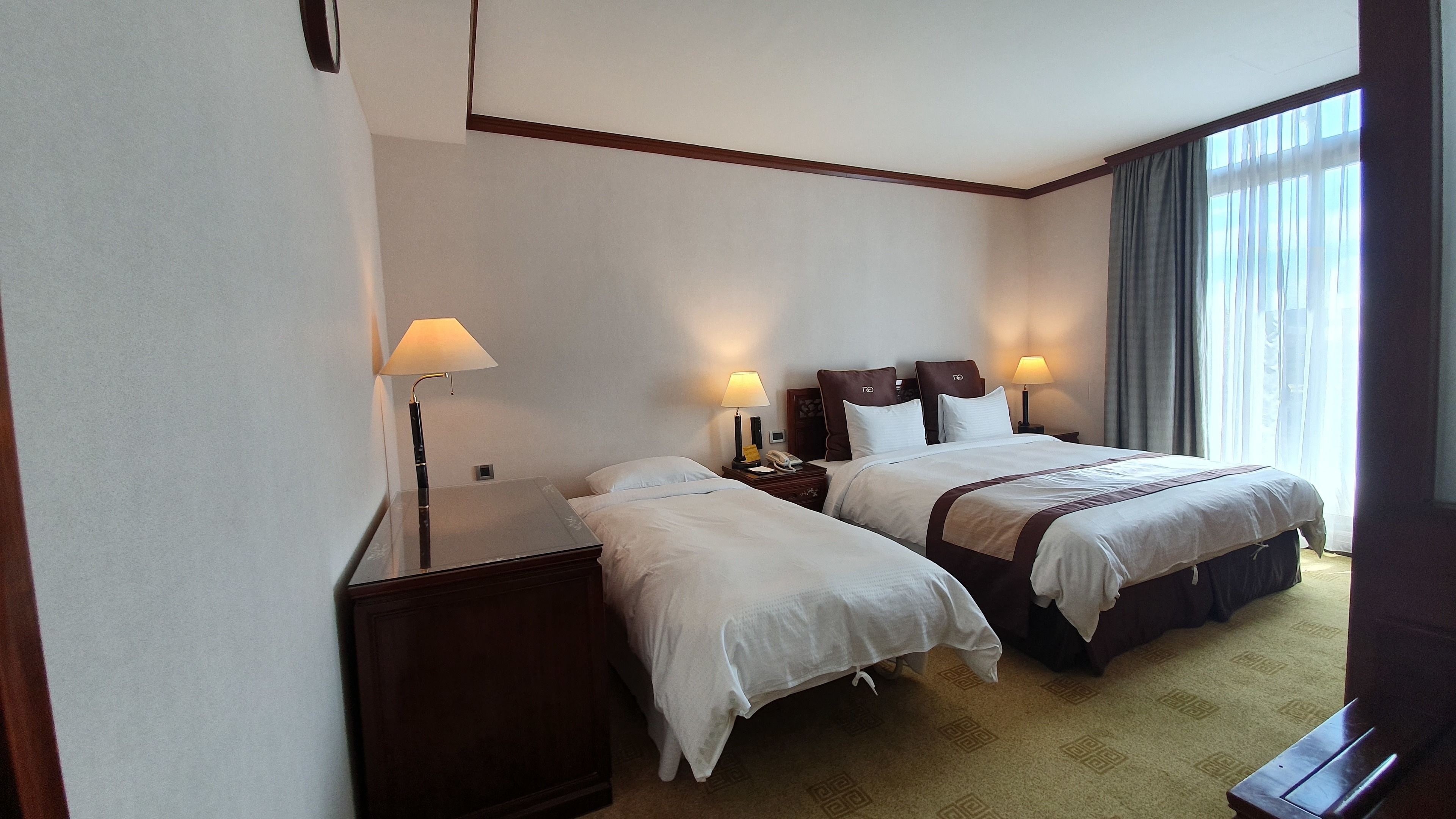 A hotel room with two beds, a desk, and a lamp.