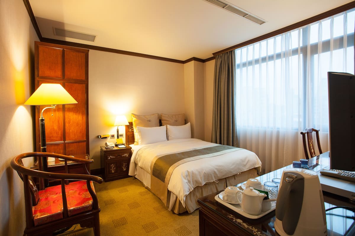 A hotel room with a bed, a desk with a computer, a chair, a lamp, and a television.