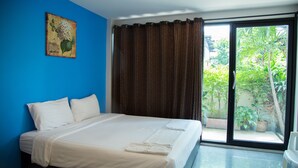 A hotel room with a large bed, a window with curtains, a painting on the wall, and a view of greenery outside. - Varinda Hostel (Bangkok)