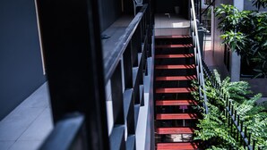 A staircase with red steps leading to a landing, surrounded by greenery and a modern building facade. - Varinda Hostel (Bangkok)