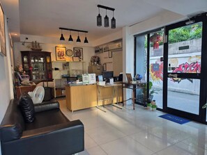 A modern reception area with a wooden desk, a black leather couch, and a large window with a view of the street. - Varinda Hostel (Bangkok)