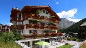 Un chalet à plusieurs étages doté de balcons en bois, d’un espace salon extérieur et offrant une vue sur les montagnes.