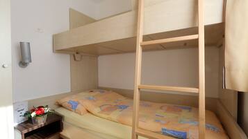 Habitación con literas de madera, una mesita con un florero y una lámpara fijada a la pared.