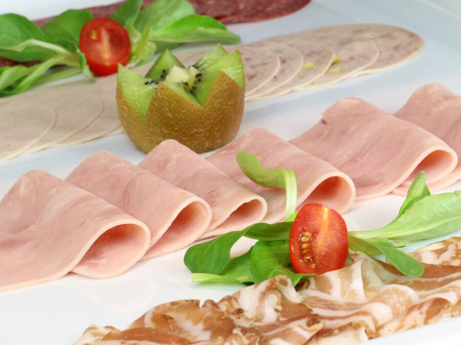 Een bord met verschillende soorten eten, waaronder vleesschijfjes, een gevuld fruit en wat groenten.