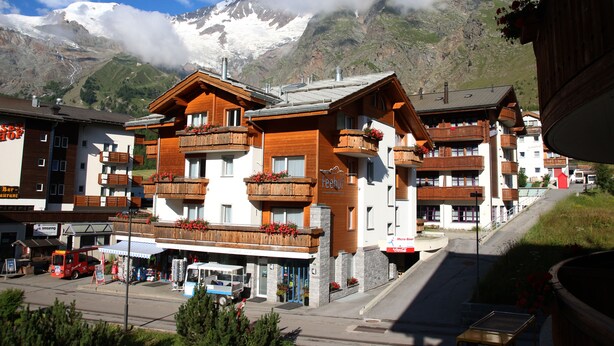 Une station de montagne avec des bâtiments en bois, des balcons ornés de jardinières et une vue sur des montagnes enneigées.