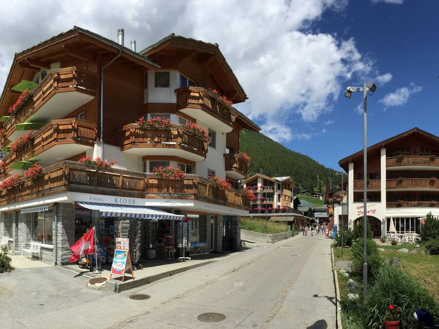 A hotel with wooden balconies, a kiosk, and a mountain backdrop.