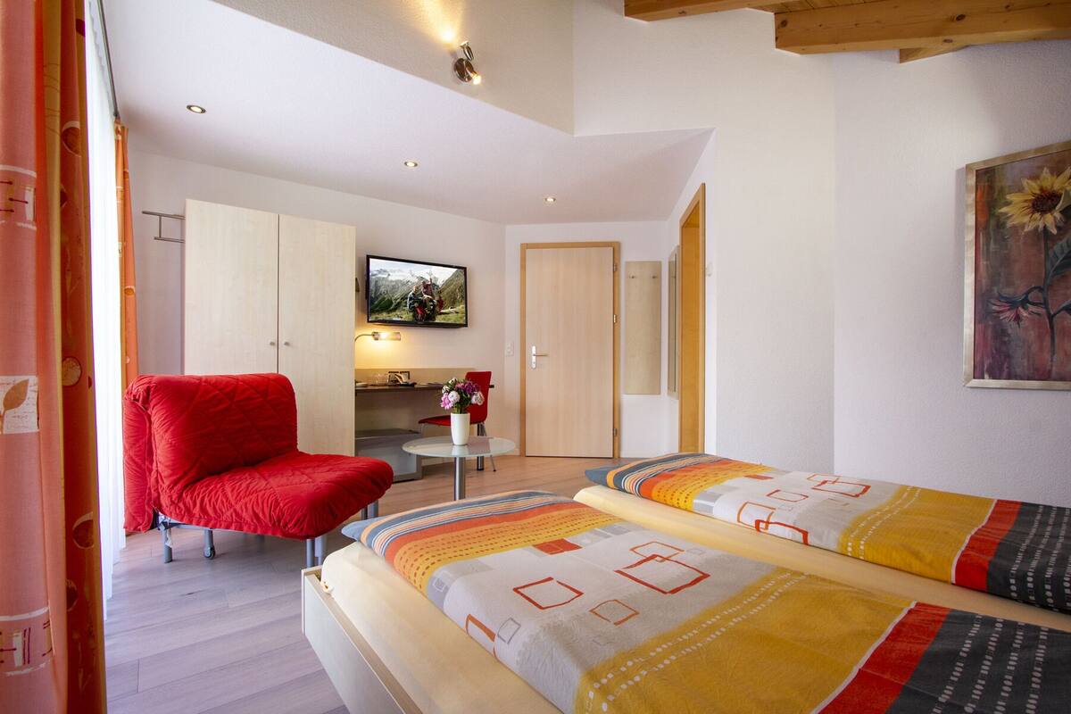 A bedroom with two beds, a red chair, a small table, a TV, and a painting.