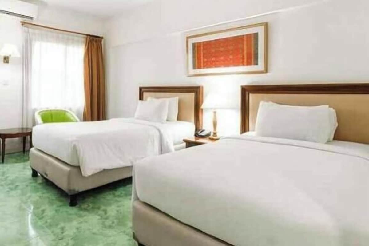A hotel room with two beds, a green carpet, a framed picture on the wall, and a chair.