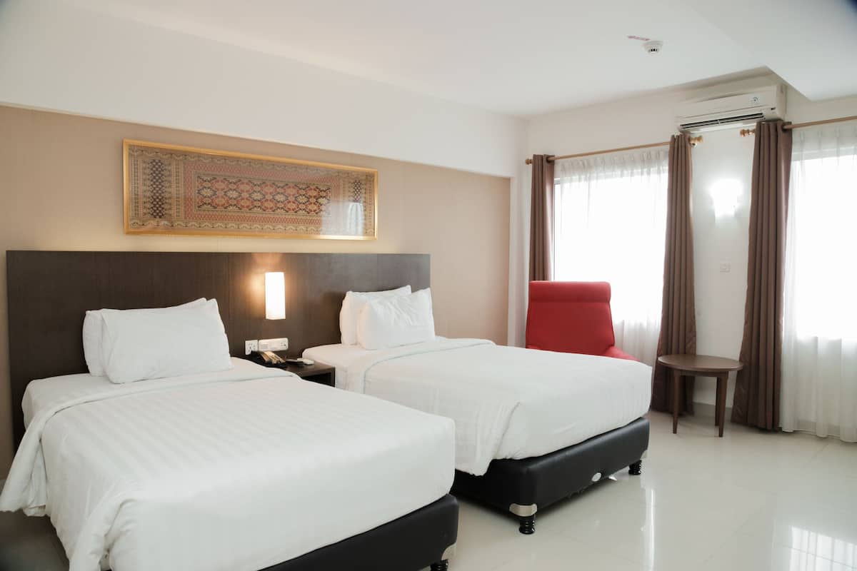 A hotel room with two beds, a red chair, a small table, and a decorative wall hanging.
