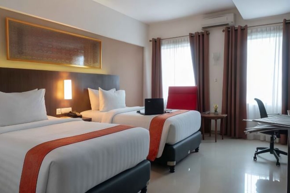 Habitación de hotel con dos camas, un escritorio, una silla y una computadora portátil.