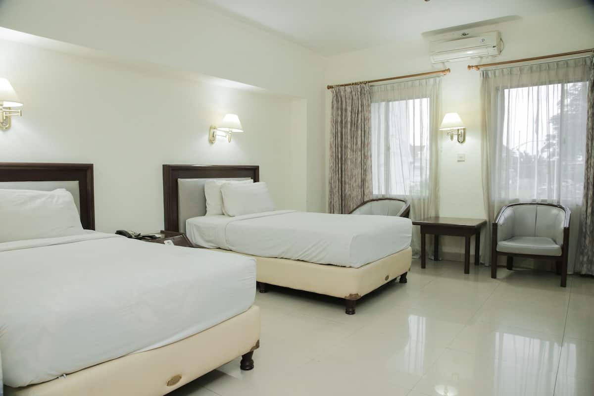 A hotel room with two beds, a small table, a chair, and a window with curtains.