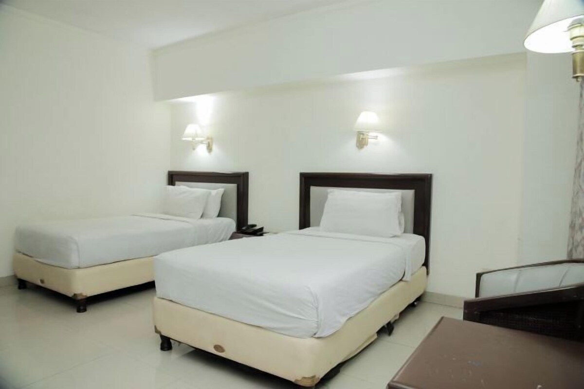 A hotel room with two single beds, a small table, and a lamp.